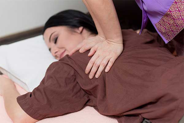 therapist applying Thai massage techniques to a woman's shoulders